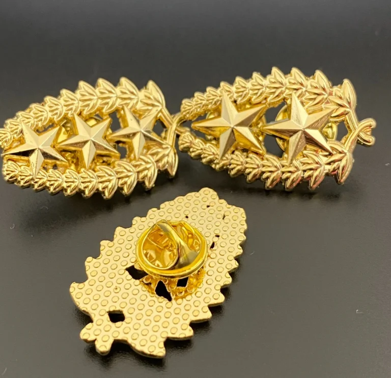 Insignias doradas con estrellas y laureles, junto a un reverso con cierre de mariposa.